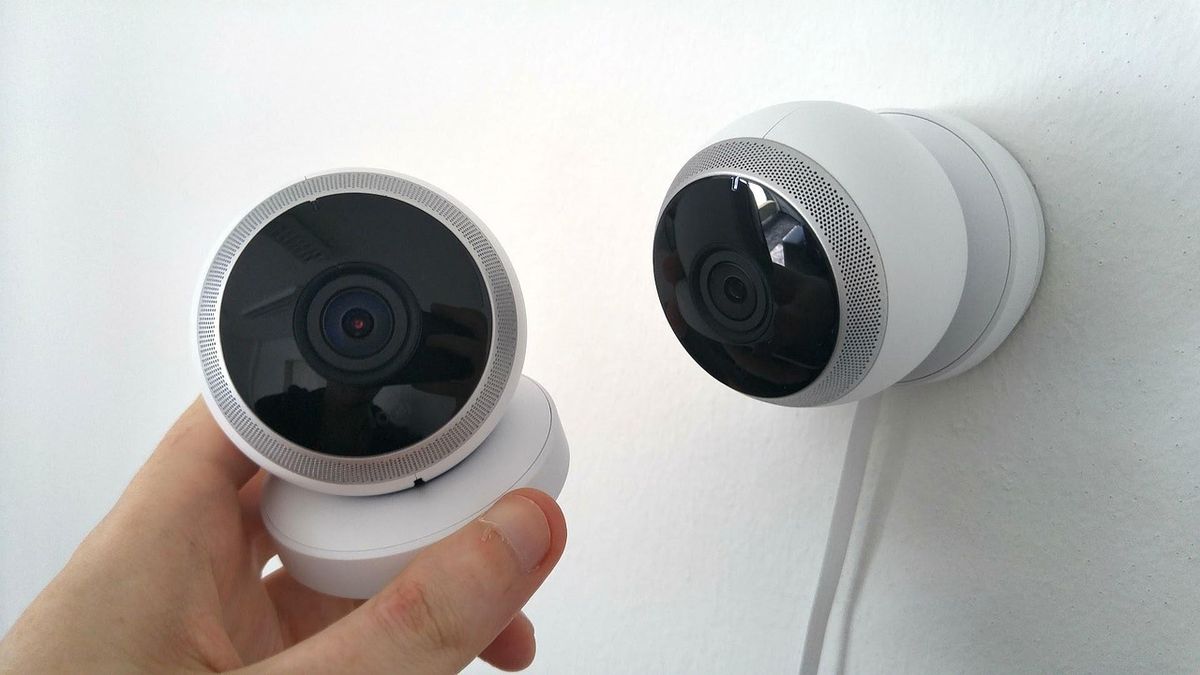 A small wireless indoor camera being held up next to a wall-mounted unit during setup