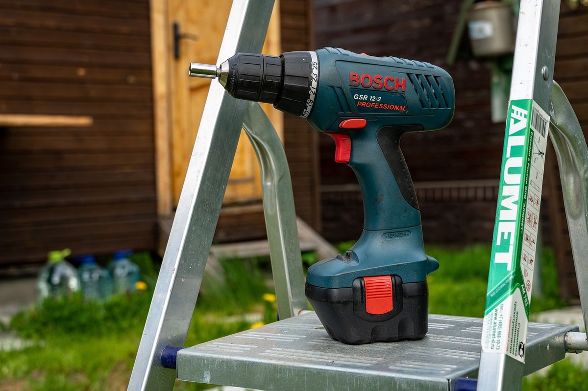 A cordless drill on a step ladder, tools used for wall-mount installation