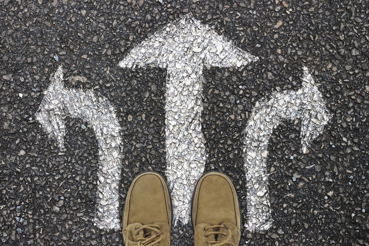 A person standing at painted directional arrows on pavement, representing a choice between options