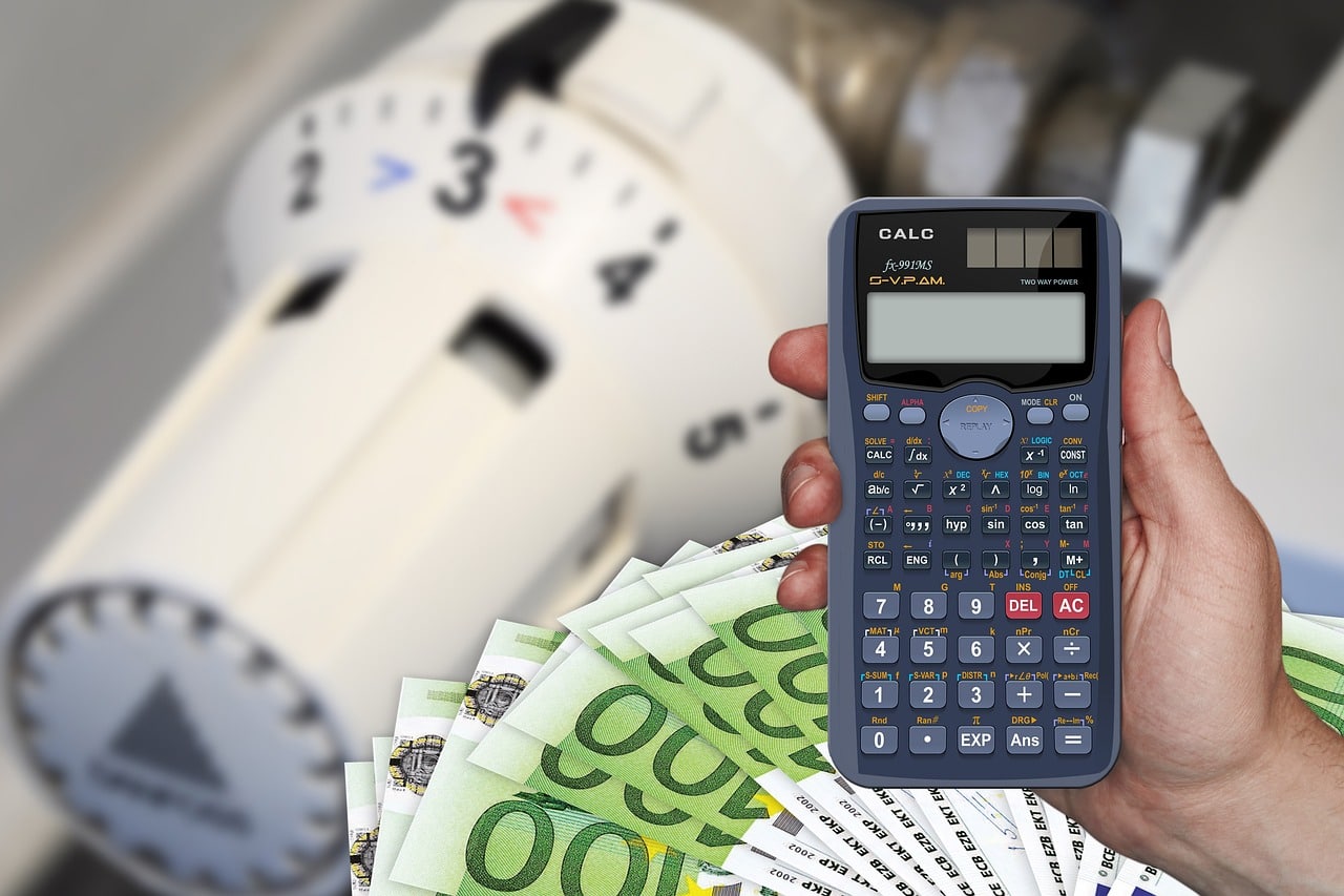 Hand holding a calculator and cash next to an old manual thermostat dial, representing calculating real energy savings