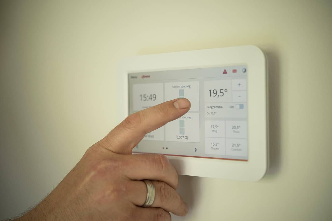 Hand adjusting a smart thermostat wall touchscreen showing temperature and energy usage