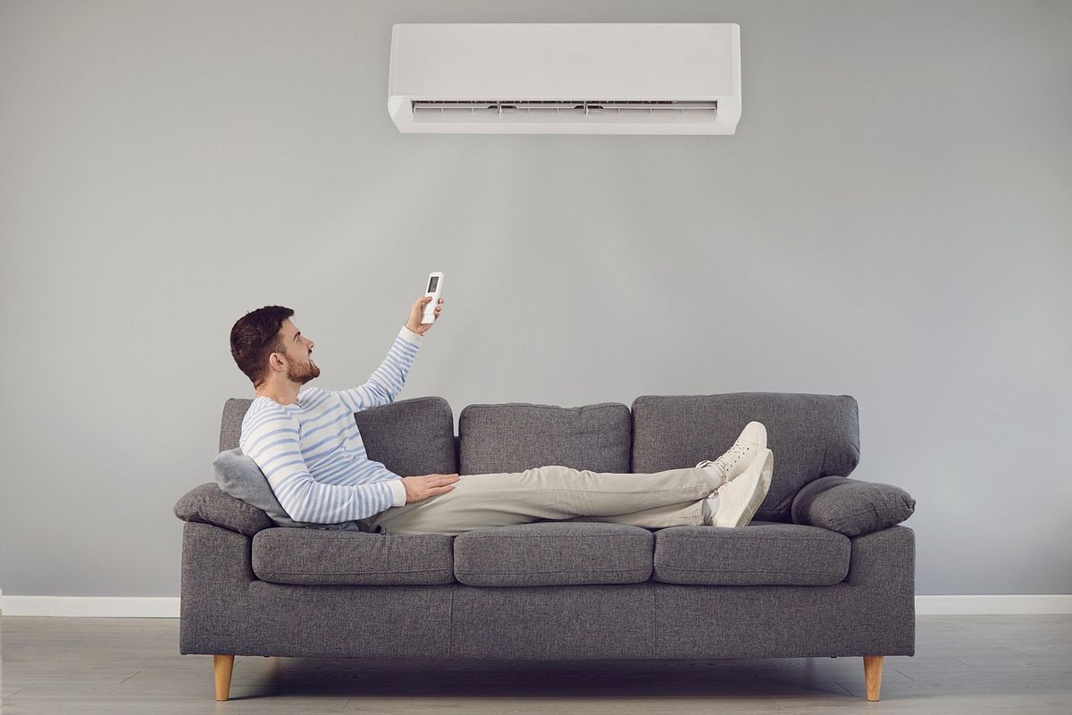 Man on a couch pointing a remote at a wall-mounted mini split air conditioner